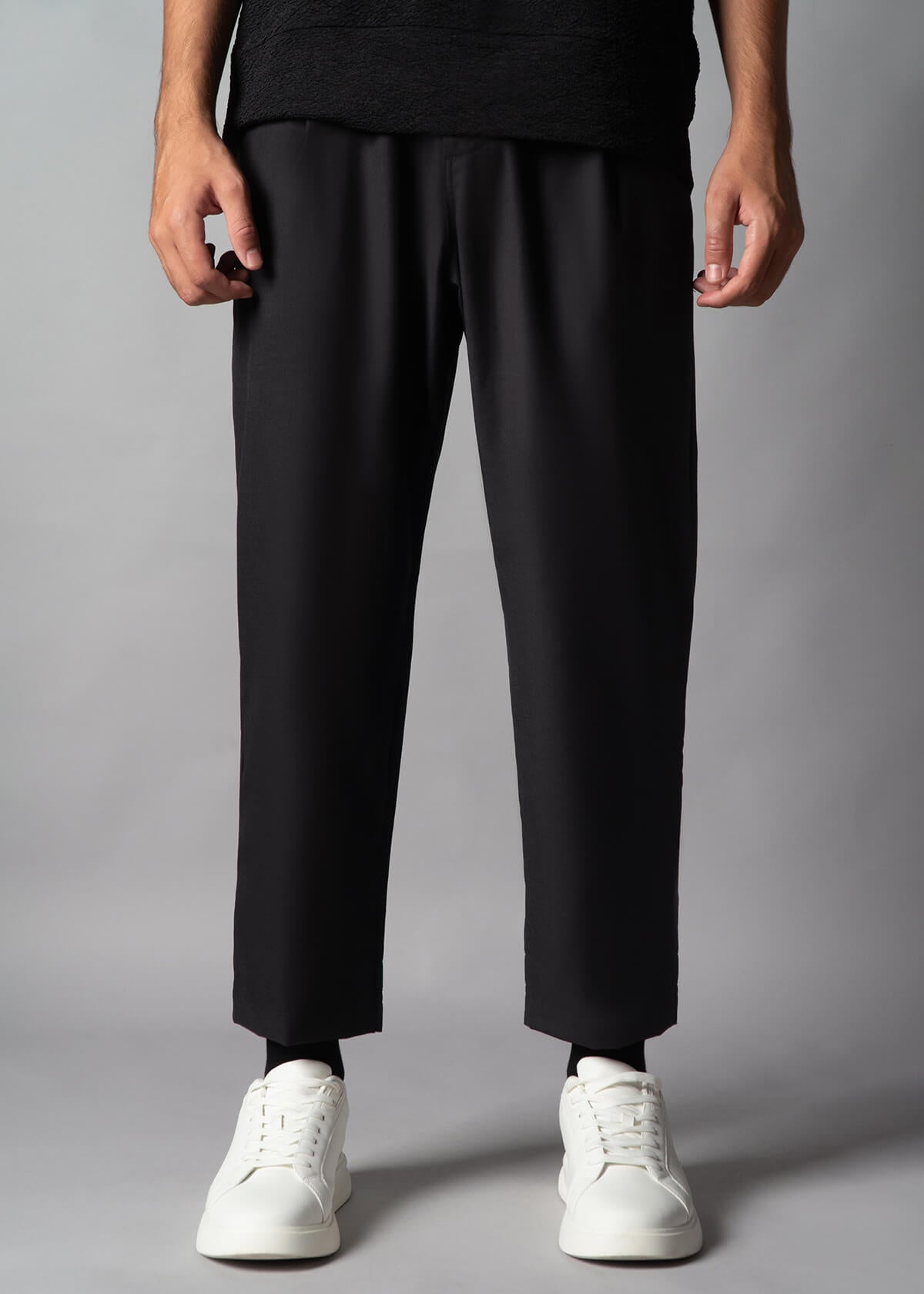 A person standing wearing black boxer-fit trousers with multiple pockets and white sneakers.